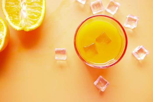orange juice and ice cube in glass on a color background .