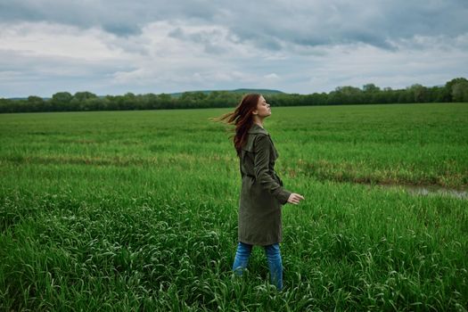 a woman stands in the middle of a green field in warm clothes. Rainy weather, walk in the forest. High quality photo