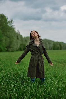 a beautiful woman stands in a field in a long raincoat enjoying nature. High quality photo