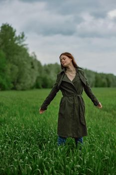 a beautiful woman stands in a field in a long raincoat enjoying nature. High quality photo