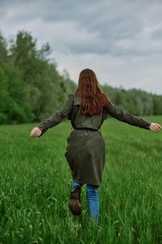 a woman in a long raincoat runs across a field in tall green grass in cloudy weather in spring. High quality photo