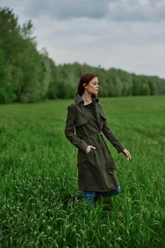 a beautiful woman in a dark coat stands in a green field in the spring in rainy weather. High quality photo