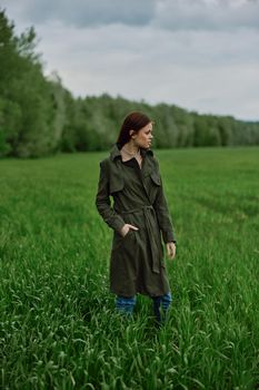 a beautiful woman in a dark coat stands in a green field in the spring in rainy weather. High quality photo