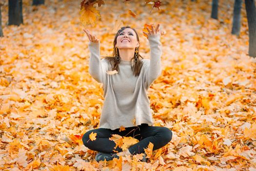 Smiling young woman having fun in autumn park playing with fallen leaves.