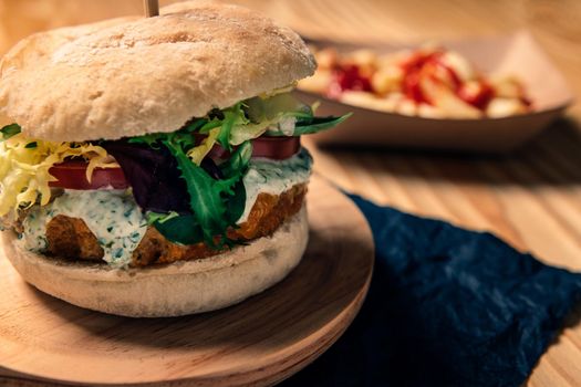 gourmet vegan burger with tomato and lettuce on a wooden table with french fries with ketchup in a cardboard tray, healthy food and foodie lifestyle concept, selective focus