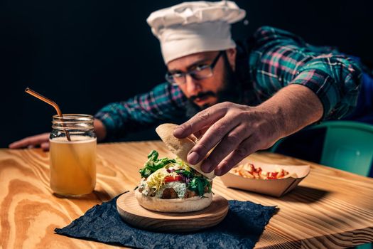chef finishing up his vegan burger with lettuce tomato and sauce, fries with ketchup and healthy drink on a wooden table, vegetarian food and foodie lifestyle concept, selective focus
