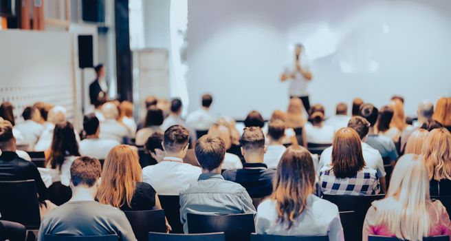 Speaker giving a talk in conference hall at business event. Rear view of unrecognizable people in audience at the conference hall. Business and entrepreneurship concept.