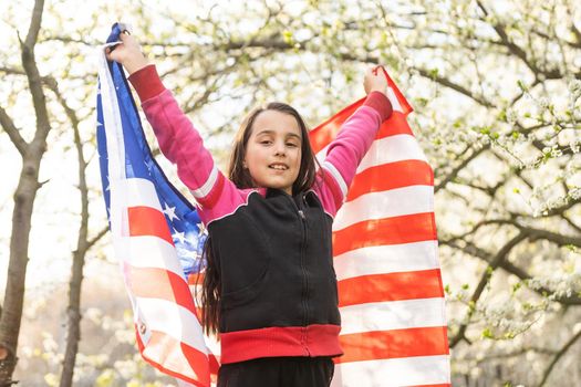 Happy adorable little girl smiling and waving American flag outside. Smiling child celebrating 4th july - Independence Day.