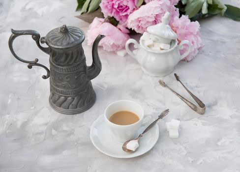 vintage still life with a cup of coffee against a bouquet of pink peonies on a gray cement background. High quality photo