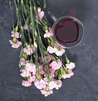pink carnations on a dark background with a cup of red tea in a heart-shaped cup, valentine's day, mother's day, gifts for loved ones. High quality photo
