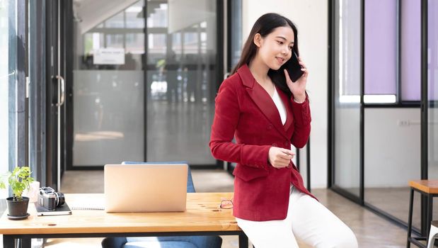 Charming Asian woman with a smile standing holding papers and mobile phone at the office..