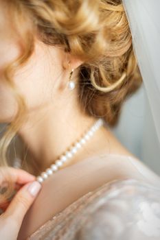 Beautiful caucasian young bride dresses necklace before wedding. Selective focus