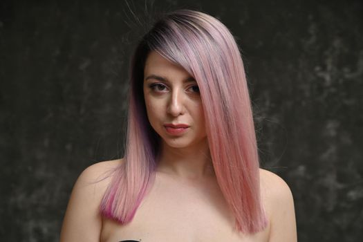 Close-up portrait of a caucasian serious girl with pink hair on a gray background