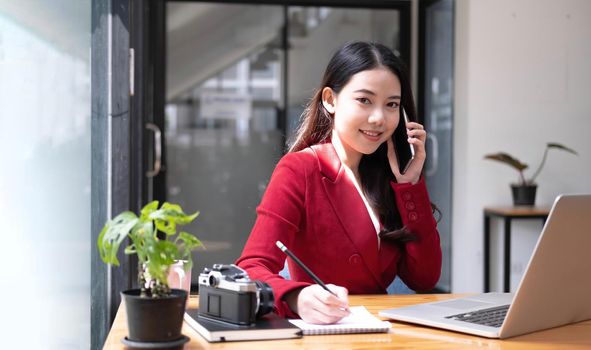 Charming Asian woman with a smile standing holding papers and mobile phone at the office..