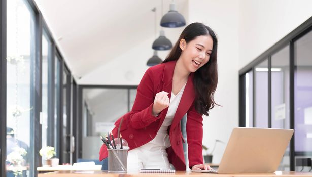 Excited happy woman looking at the phone screen, celebrating an online win, overjoyed young asian female screaming with joy at office