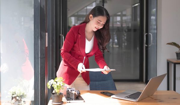 Portrait of Young Asian woman hand freelancer is working her job on computer tablet in modern office. Doing accounting analysis report real estate investment data, Financial and tax systems concept..