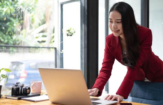 Portrait of Asian young female Businesswoman working on laptop computer doing finances,accounting analysis,report,data and pointing graph at the office..