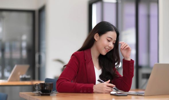 Beautiful Asian businesswoman analyzes charts using laptop calculator at the office..