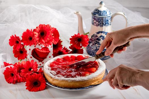 Still life, a woman cuts a strawberry pie on a table decorated with red gerberas, mother's day, birthday