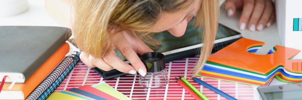 Close-up of busy professional interior designer choose colour to cover walls. Woman use magnifying glass tool to look through palette. Art, design concept