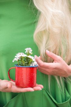 a blonde girl with long hair in a bright green dress holding a red mug with a bouquet of white flowers, portrait, High quality photo