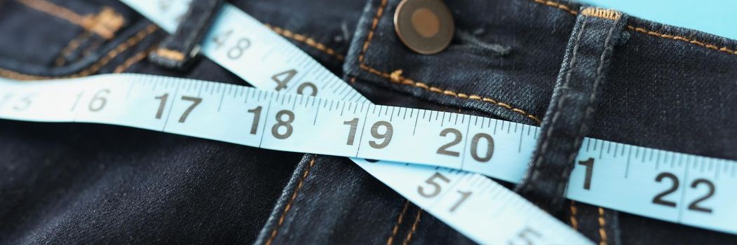 Close-up of denim trousers or jeans with blue measure tape around waist. Sew clothes for your individual order. Atelier, weight loss, business concept