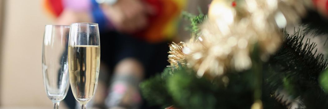 Close-up of two glasses near decorated christmas tree and sad woman sitting alone. Broke up with girlfriend on new year. Christmas holiday, lgbt concept