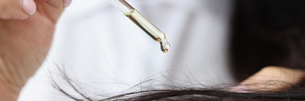 Close-up of girl hold dropper with castor extract oil near hair and apply one drop. Long hair care routine, oil for head. Wellness, beauty ritual concept