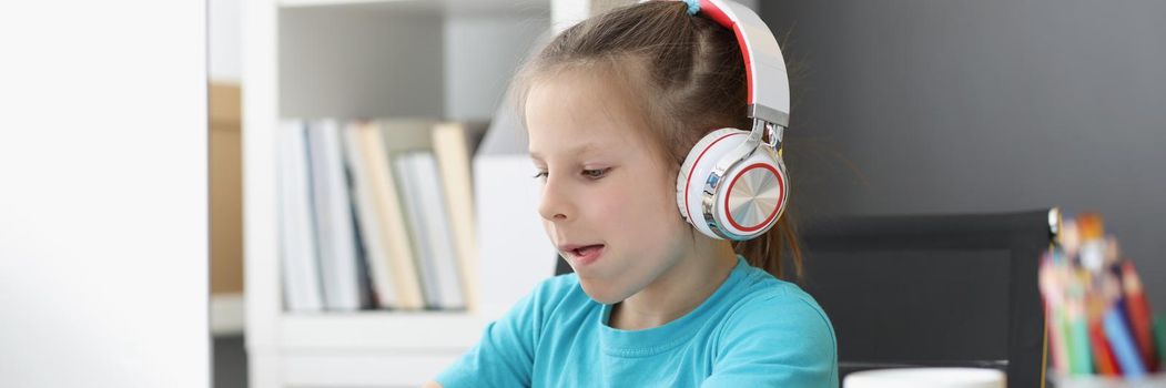 Portrait of cute kid wearing headset and typing on keyboard with effort. Child explore new technology, try computer in use. Childhood, development concept