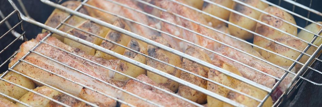Close-up of raw vegetable and slices of meat cooking on grill outdoors. Potatoes and lard in barbecue. Nature, bbq, picnic, lunch on fresh air concept