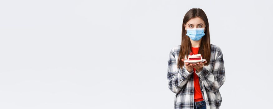 Coronavirus outbreak, lifestyle during social distancing and holidays celebration concept. Young cute girl in medical mask and casual outfit, holding birthday cake and looking serious camera.