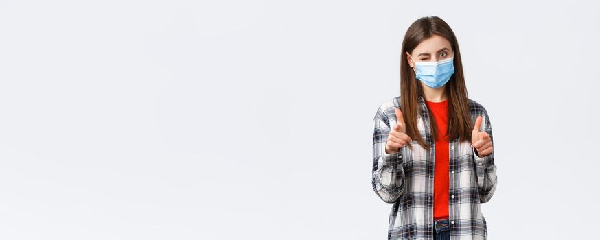 Coronavirus outbreak, leisure on quarantine, social distancing and emotions concept. You can dot it. Supportive young attractive female in medical mask pointing at camera, wink and congratulate.