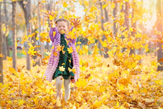 Joyful laughing caucasian girl having fun in autumn park throws up fallen leaves.