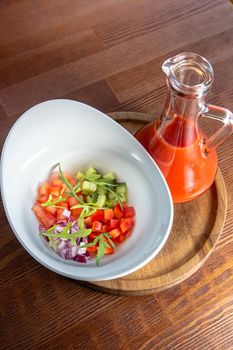 Tasty appetizing summer tomato soup puree gazpacho with tomatoes and cucumbers served in bowl on wooden background.