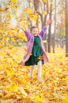 Smiling caucasian girl having fun in autumn park throws up fallen leaves.