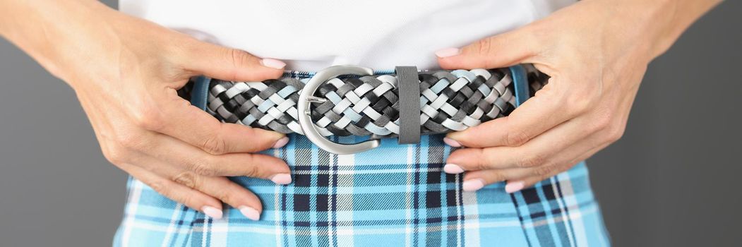 Close-up of woman touching new trendy belt wearing with plaid printed skirt. Female in fashionable look posing in studio. Fashion, trend, style concept