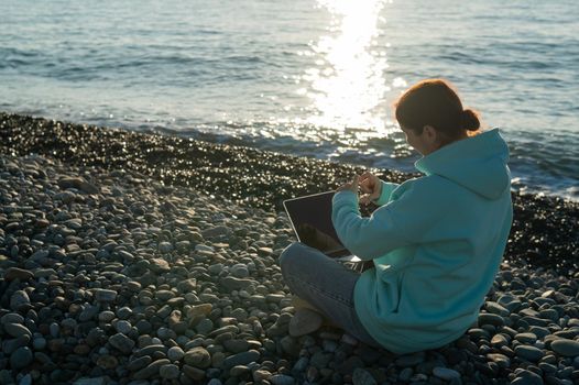 Caucasian woman communicating by video call on laptop on pebble beach