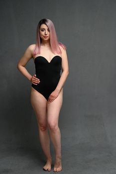 Full length portrait of a caucasian girl with pink hair in a black bodysuit on a gray background