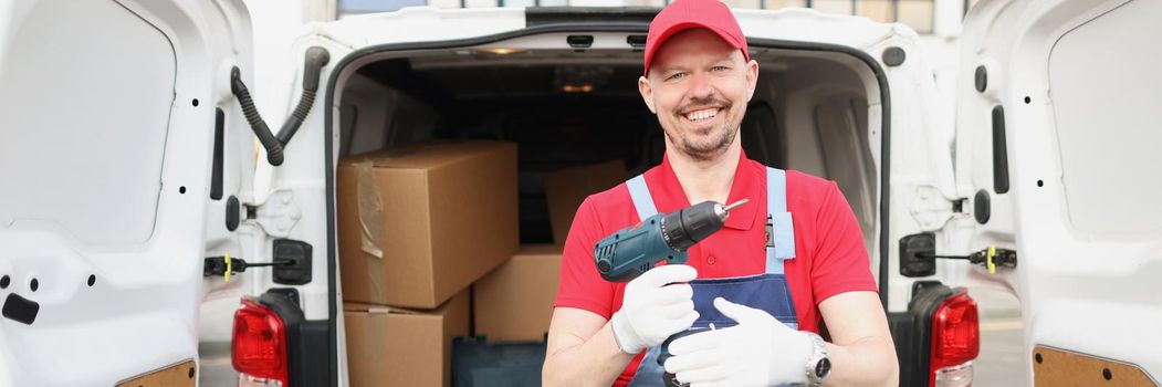 Portrait of smiling worker hold screwdriver device in hand in front of truck full of boxes. Man help to fix things or with moving. Handyman service concept