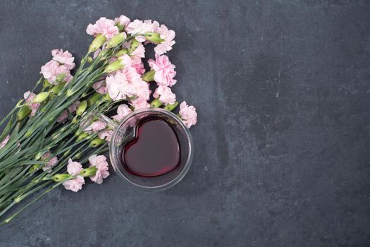 pink carnations on a dark background with a cup of red tea in a heart-shaped cup, valentine's day, mother's day, gifts for loved ones. High quality photo