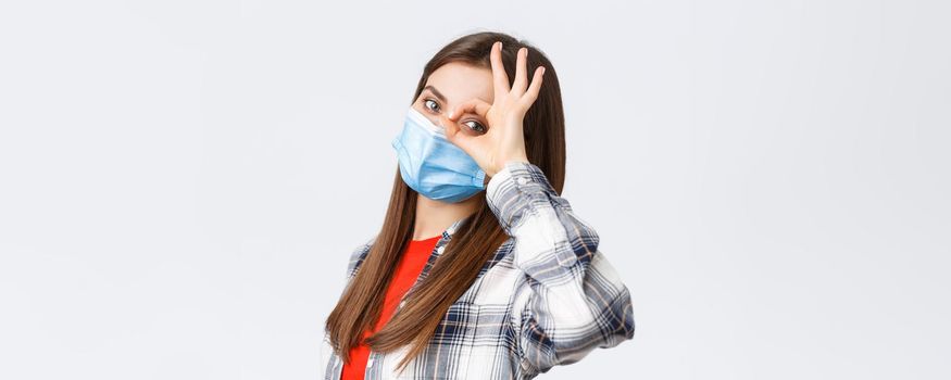 Coronavirus outbreak, leisure on quarantine, social distancing and emotions concept. Dreamy cute girl in medical mask, showing all okay, everything good, make OK sign over eye.