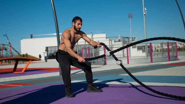 Shirtless man doing exercises with ropes outdoors