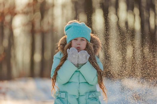 little girl blows on the snow that is on her mittens