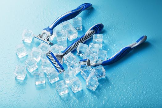 Blue shaving machines in a row on a blue background with ice cubes. The concept of cleanliness and frosty freshness