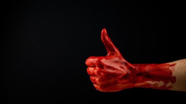 A woman's hand stained with blood shows a thumbs up on a black background