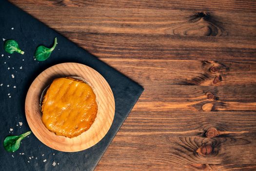 top view of a vegan burger with melted cheese on a wooden plate in a slate tray with green leaves, wood background, vegan food and healthy lifestyle concept