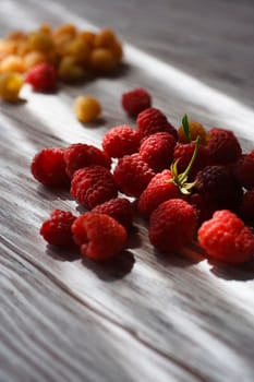 Two handfuls of fresh red and yellow raspberry on white wooden table, selective focus.