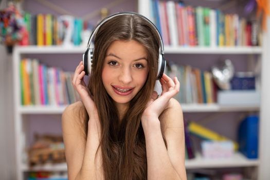 Sympathetic teenage girl with headphones on her ears. Young cheerful brunette is listening to music on wireless headphones.