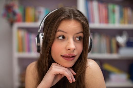 A cheerful young girl is listening to music through headphones. She perversely looks to the side. Close-up view of attractive brunette with long hair.