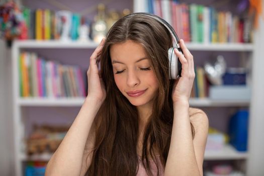 Young brunette girl listens to music with wireless headphones. A teenage girl with her eyes closed. Attractive girl with long hair.